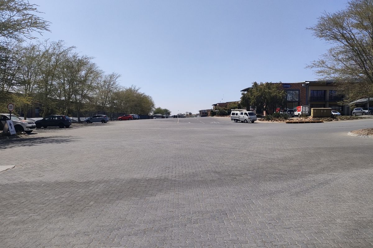 A wide-angle view of a paved industrial parking lot and driveway area with surrounding trees and commercial building access.