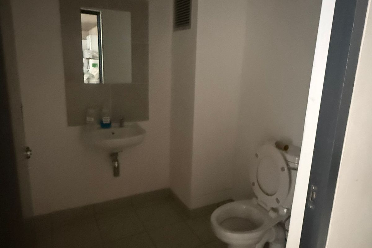 A functional industrial restroom featuring a wall-mounted basin, mirror, and standard toilet fixture with tiled flooring.