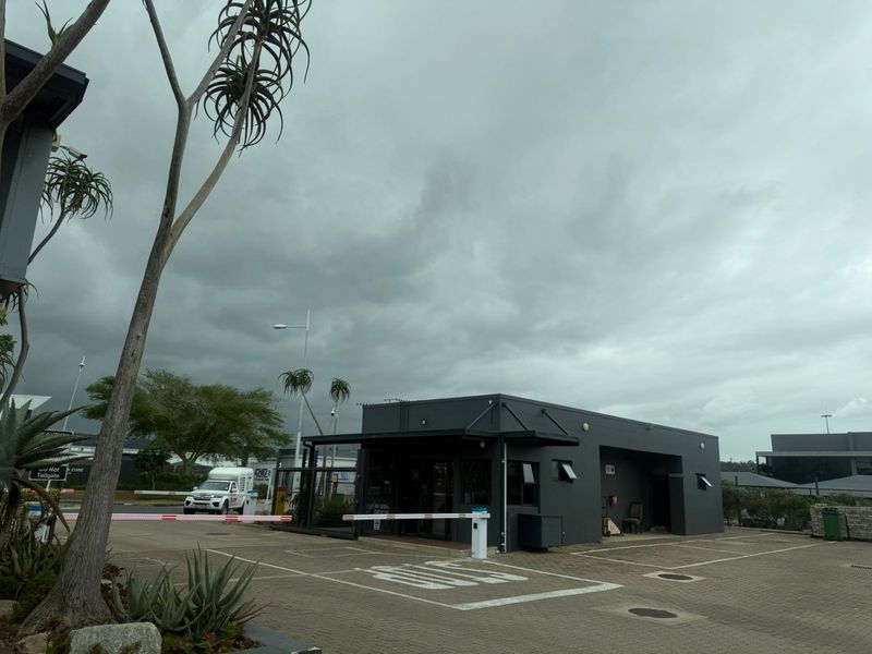Exterior view of a modern industrial security gatehouse featuring a paved driveway, boom gate access control, and dark grey exterior finish.