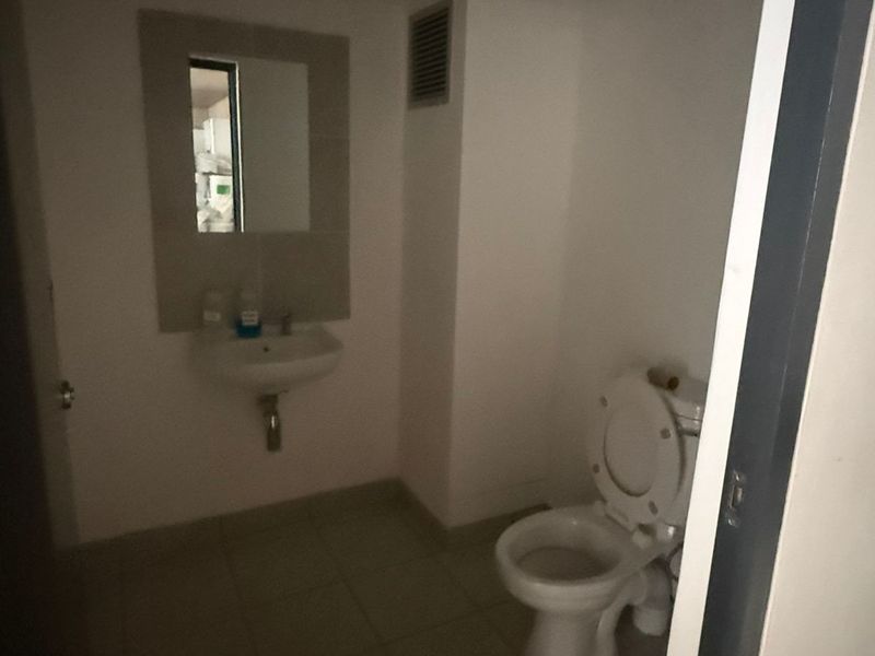 A functional industrial restroom featuring a wall-mounted basin, mirror, and standard toilet fixture with tiled flooring.
