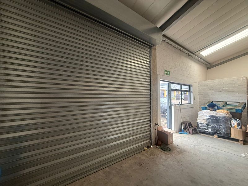 Industrial warehouse space featuring a large metal roller shutter door, exposed ceiling beams, and a separate pedestrian access door.