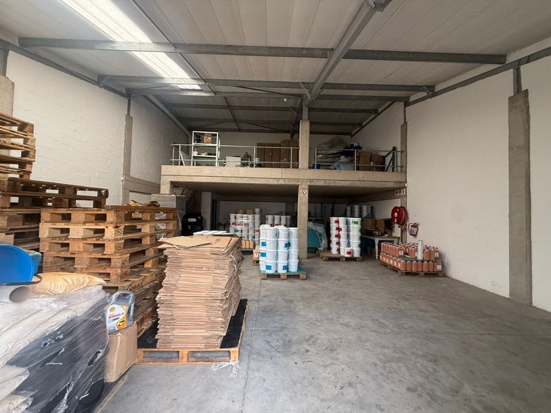 Industrial warehouse space featuring a concrete floor, exposed steel roof structure, and a mezzanine level for additional storage or office potential.