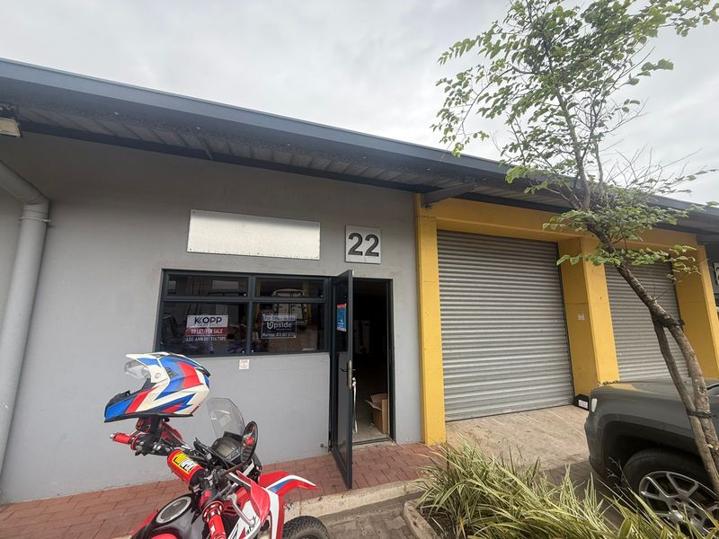 Industrial unit entrance featuring a roller shutter door, glass window frontage, and clear unit number signage.