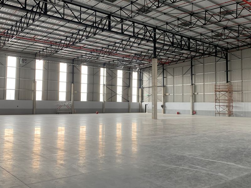 Spacious industrial warehouse featuring high ceilings with exposed steel trusses, polished concrete floors, and abundant natural light through vertical windows.