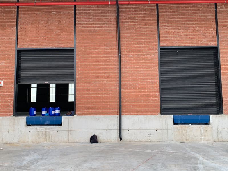Industrial loading bay area featuring two roller shutter doors, dock levelers, and a durable concrete apron with exposed brick exterior wall.
