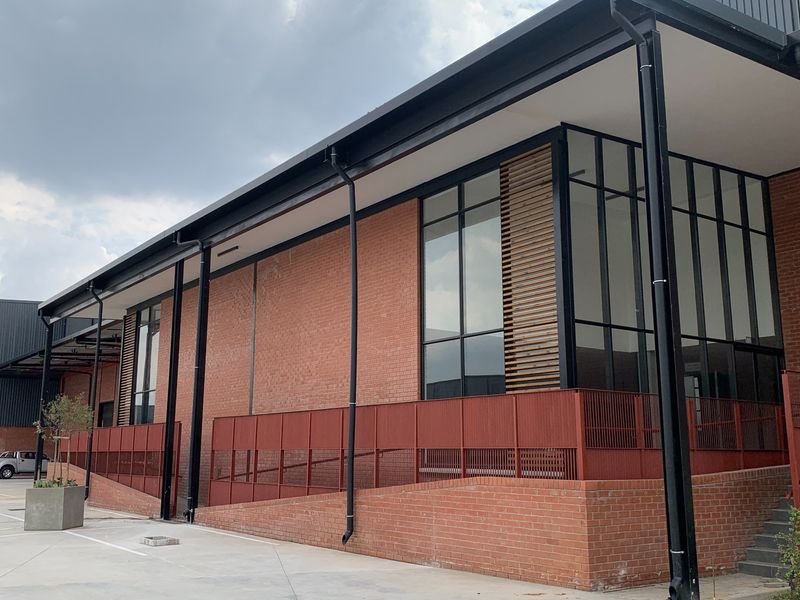 Modern industrial building exterior featuring red brick facade, large steel-framed windows with timber louvres, and a functional brick ramp access.