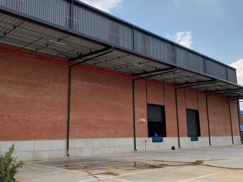 Industrial warehouse exterior featuring exposed brickwork, concrete base, metal cladding, and functional loading bays with roller shutter doors.