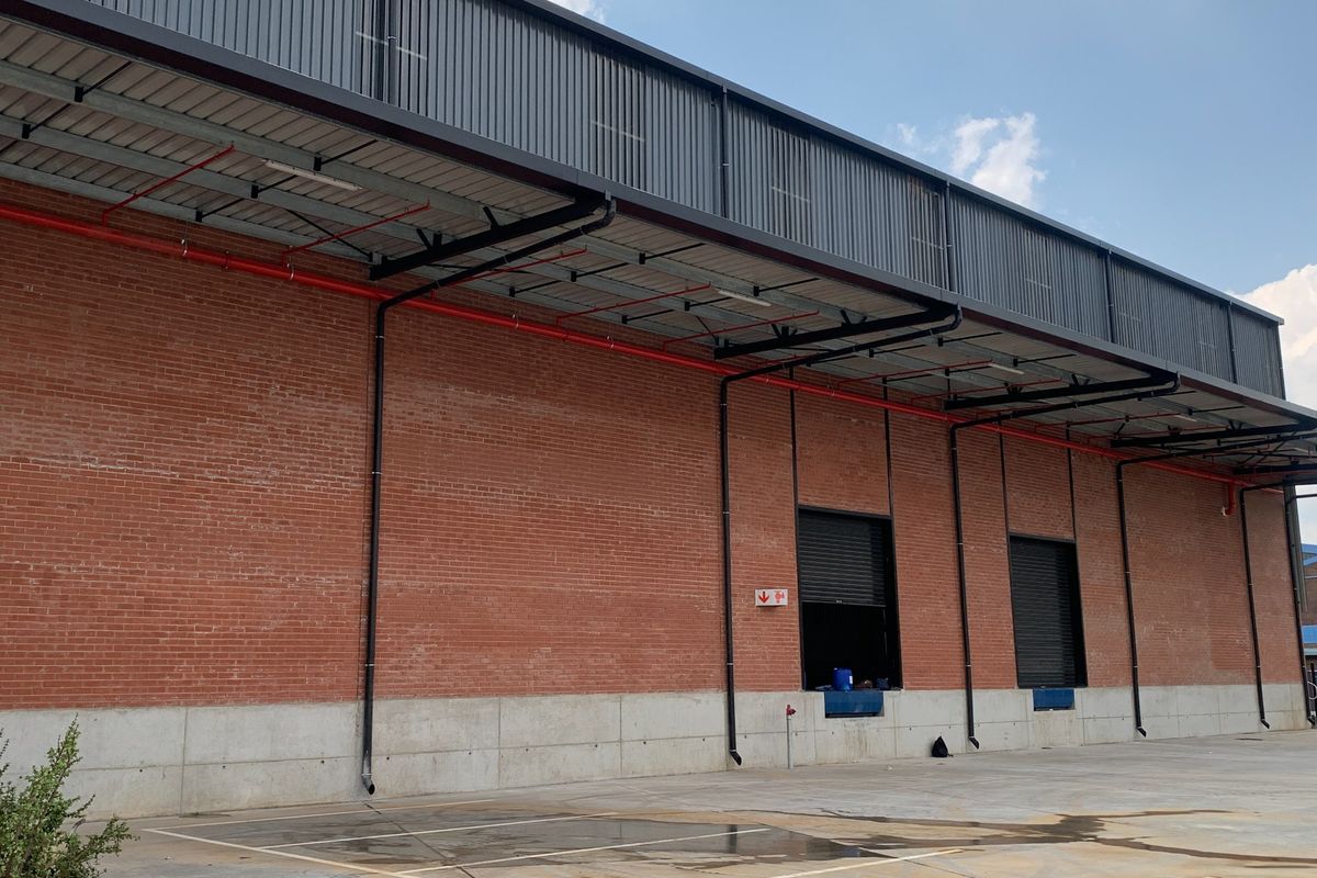 Industrial warehouse exterior featuring exposed brickwork, concrete base, metal cladding, and functional loading bays with roller shutter doors.