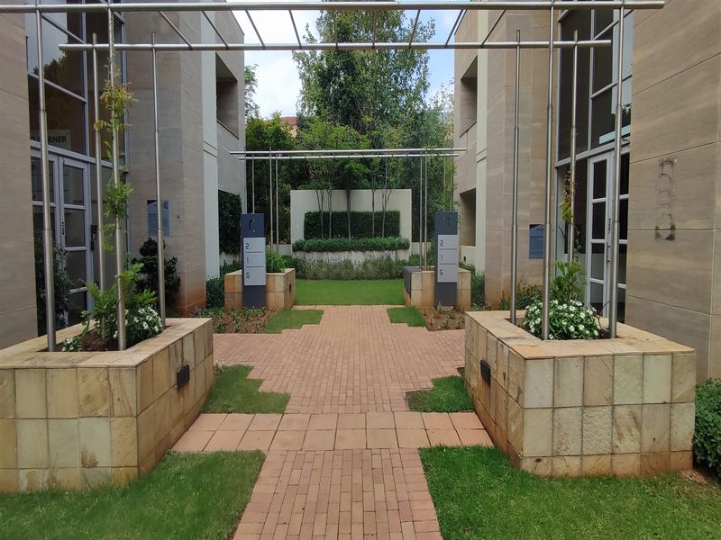 A well-maintained office courtyard featuring paved walkways, stone planters, and modern metal pergolas between two professional office buildings.