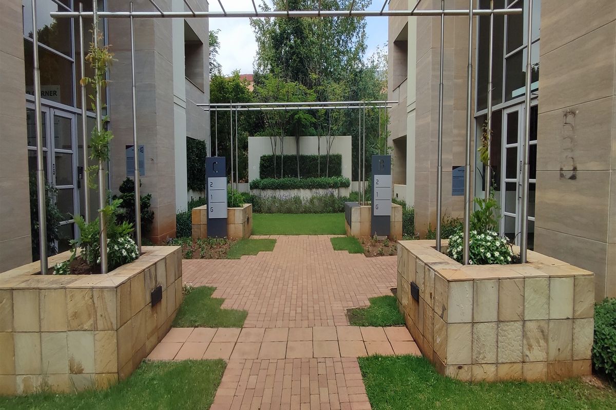 A well-maintained office courtyard featuring paved walkways, stone planters, and modern metal pergolas between two professional office buildings.