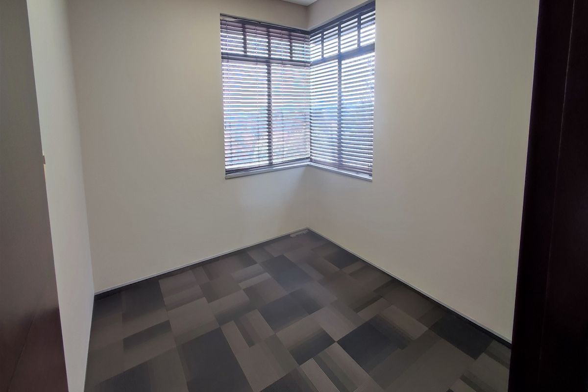 A clean, empty office space featuring modern carpet tiles and a corner window with fitted venetian blinds, offering a bright and professional work environment.