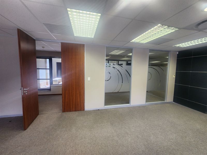 A vacant office space featuring carpeted flooring, suspended ceilings with recessed lighting, and glass partitions providing a professional, open-plan feel.