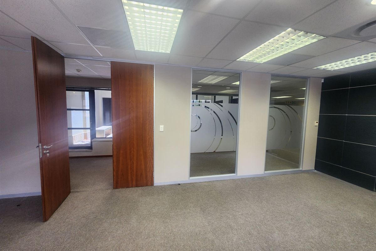 A vacant office space featuring carpeted flooring, suspended ceilings with recessed lighting, and glass partitions providing a professional, open-plan feel.