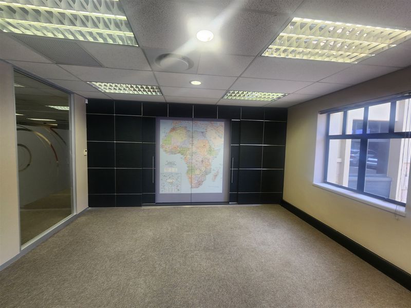 A clean, empty office space featuring a suspended ceiling with recessed lighting, carpeted flooring, and a modern glass partition wall.