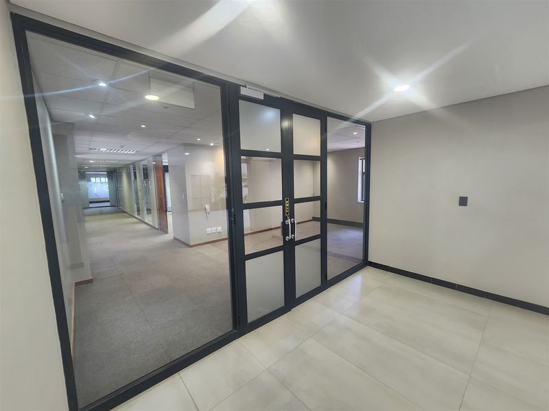 Modern office space featuring a glass partition with black metal framing, recessed lighting, and a combination of tiled and carpeted flooring.