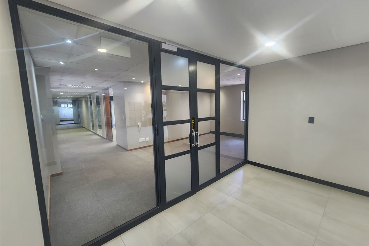 Modern office space featuring a glass partition with black metal framing, recessed lighting, and a combination of tiled and carpeted flooring.