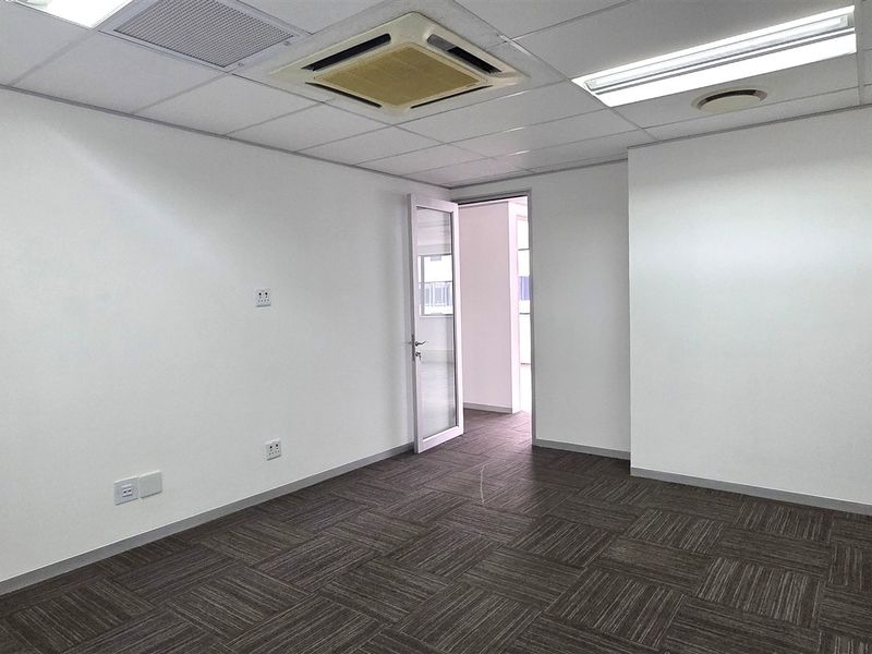 A clean, empty office space featuring neutral carpet tiles, a suspended ceiling with integrated air conditioning, and recessed lighting.