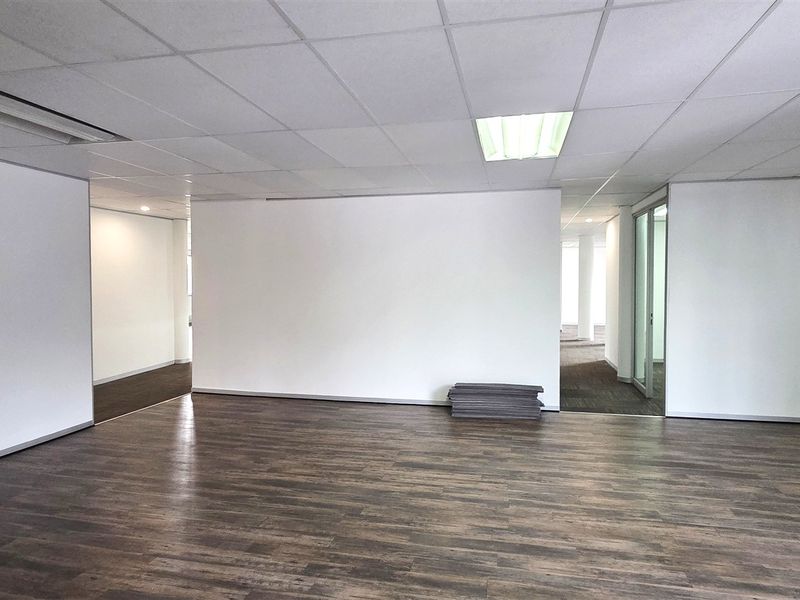 A spacious, empty office area featuring a suspended ceiling with recessed lighting and dark wood-look laminate flooring, offering a clean and professional workspace.