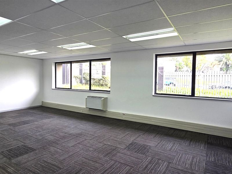 A bright, open-plan office space featuring carpet tiles, a suspended ceiling with recessed lighting, and wall-mounted air conditioning.