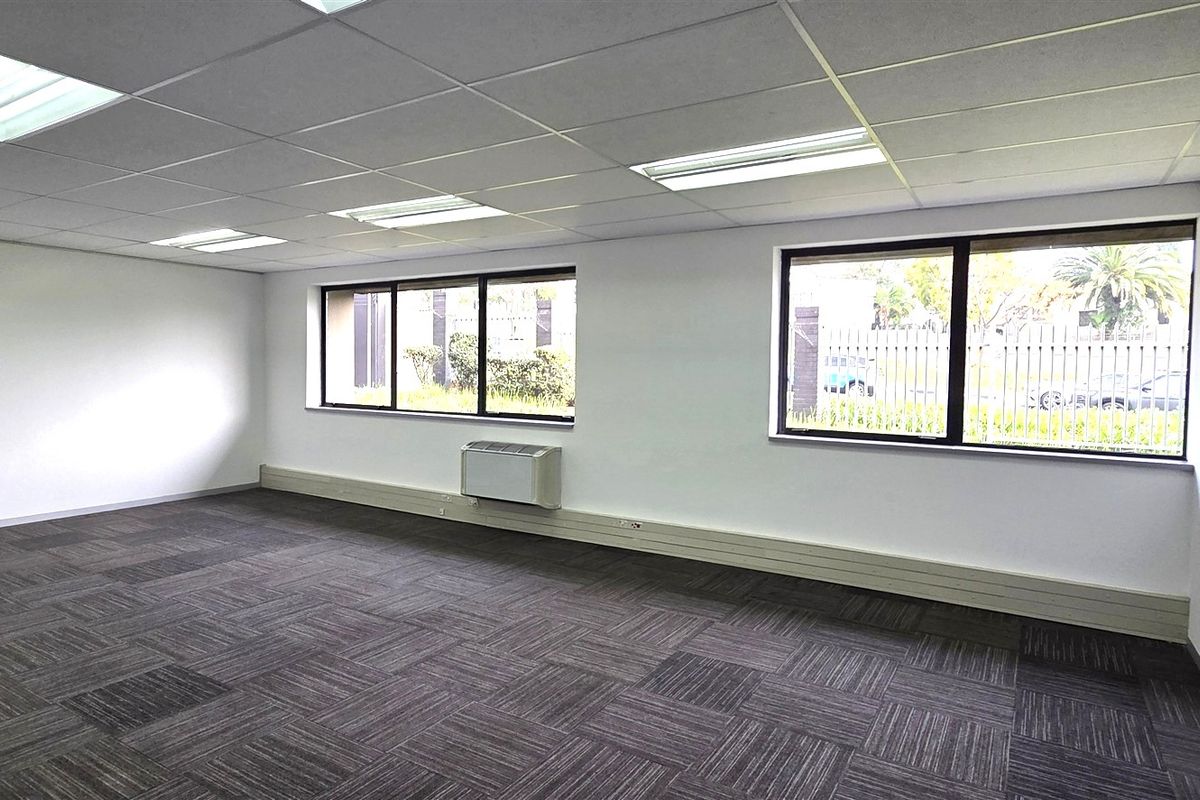 A bright, open-plan office space featuring carpet tiles, a suspended ceiling with recessed lighting, and wall-mounted air conditioning.