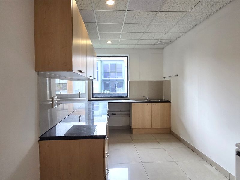 A clean, functional office kitchen featuring light wood cabinetry, dark stone countertops, tiled flooring, and a drop ceiling with recessed lighting.