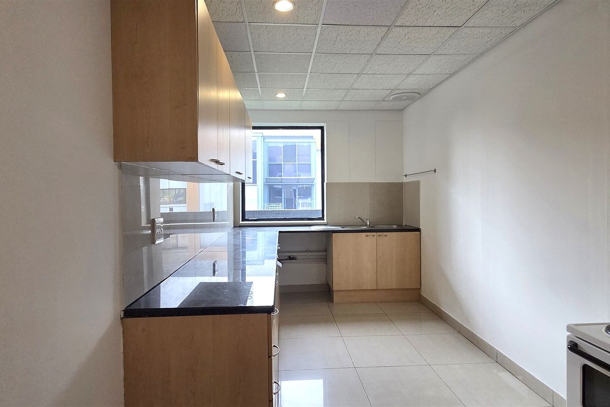 A clean, functional office kitchen featuring light wood cabinetry, dark stone countertops, tiled flooring, and a drop ceiling with recessed lighting.