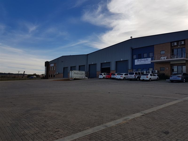 Front exterior view of an industrial warehouse facility featuring multiple roller shutter doors, brick and metal cladding, and a large paved parking area.
