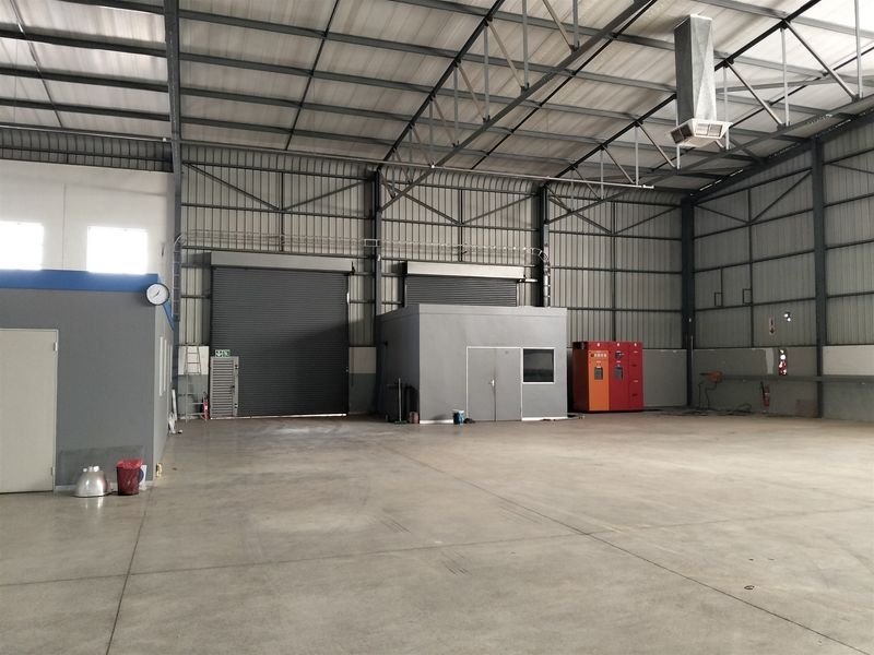 Spacious industrial warehouse featuring high ceilings with exposed steel trusses, concrete flooring, roller shutter doors, and integrated office partitioning.