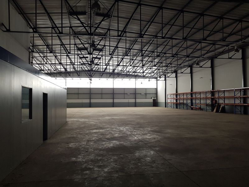 Spacious industrial warehouse featuring high-clearance steel roof trusses, durable concrete flooring, integrated racking systems, and a partitioned internal office space.