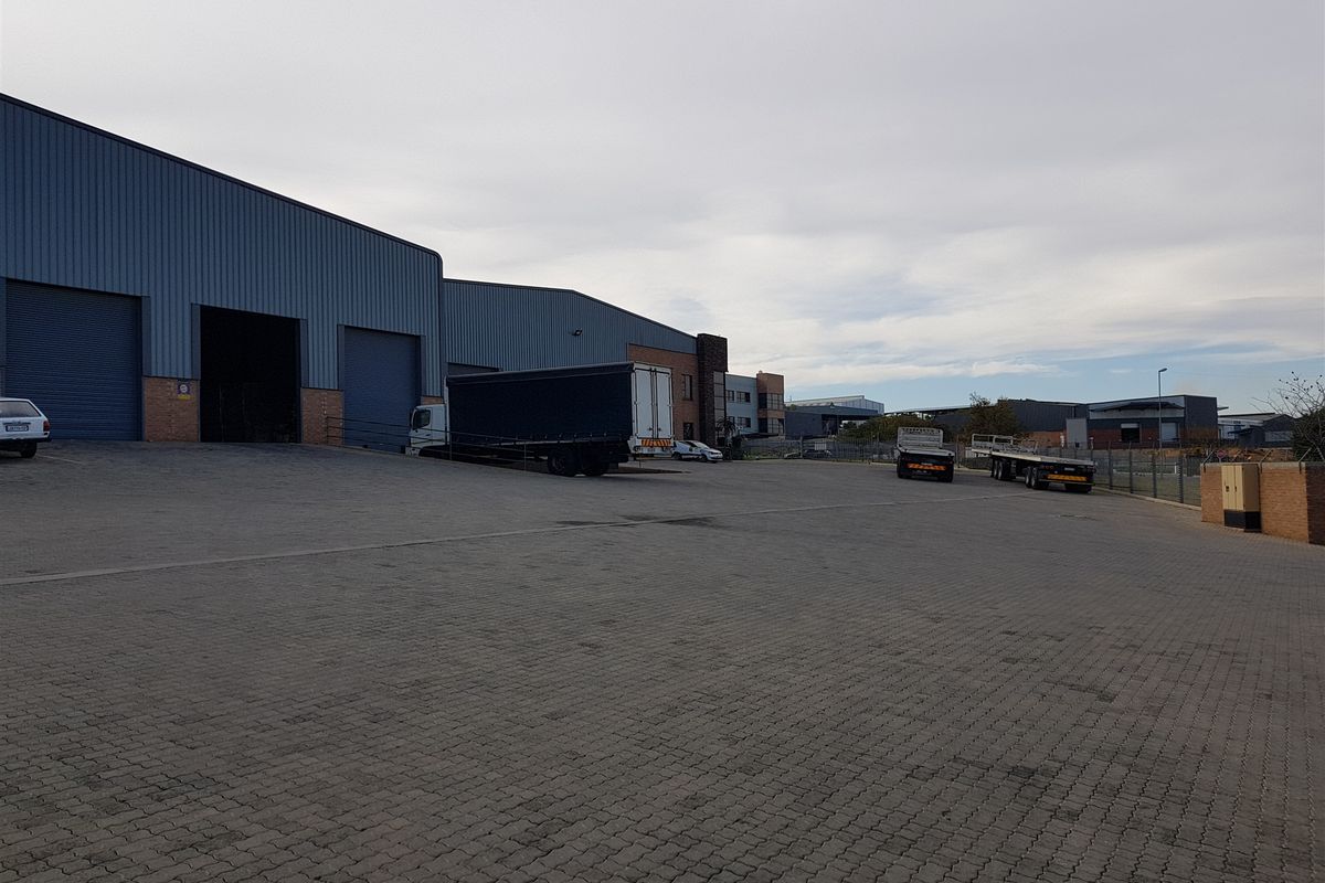 Industrial property featuring a large paved yard, multiple roller shutter doors, and metal cladding, suitable for logistics or manufacturing operations.