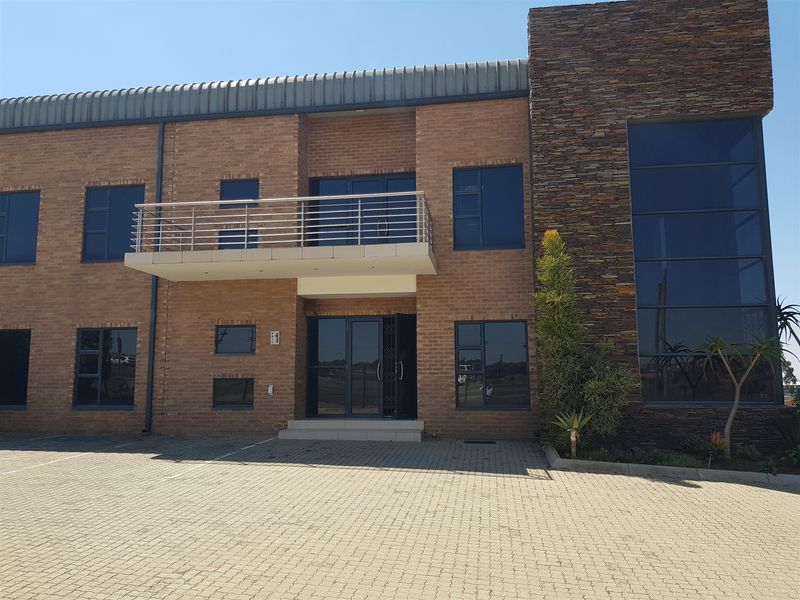 Modern industrial office building featuring a face brick facade, stone cladding accents, large glass windows, and a private balcony.