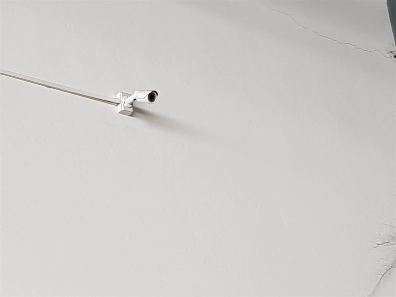 A close-up view of a wall-mounted security camera showing visible structural cracking on the wall surface.