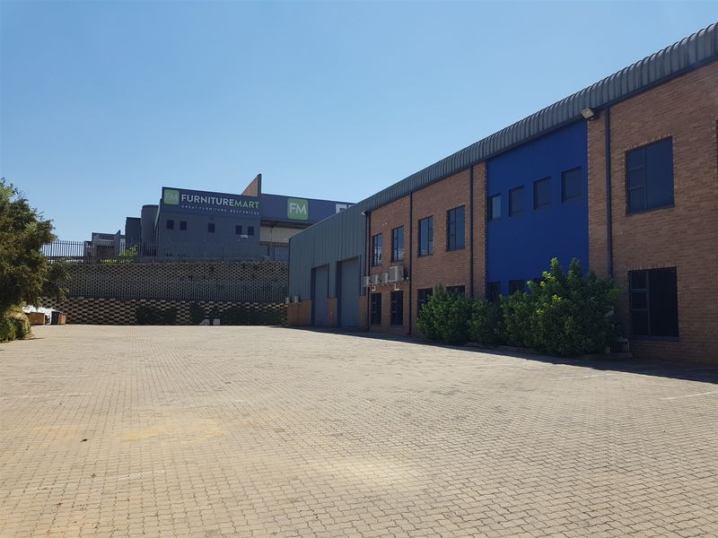Spacious industrial exterior featuring a paved parking area, brick facade, roller shutter doors, and external air conditioning units.