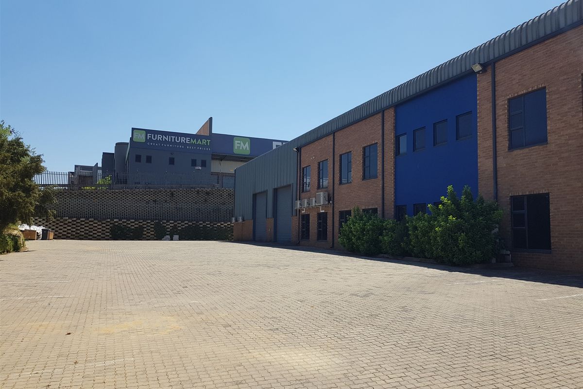 Spacious industrial exterior featuring a paved parking area, brick facade, roller shutter doors, and external air conditioning units.