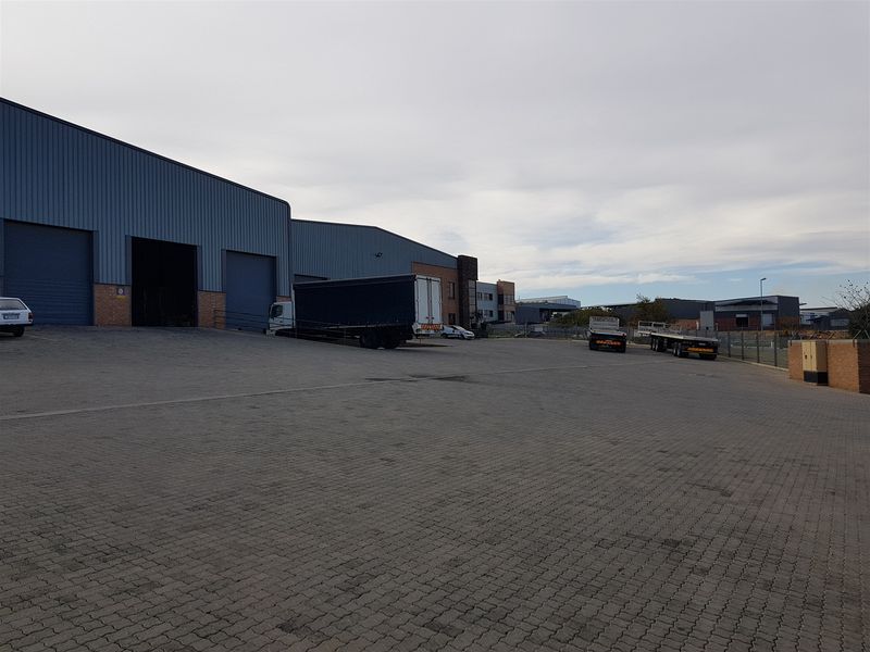 Industrial property featuring a large paved yard, multiple roller shutter doors, and metal cladding, suitable for logistics or manufacturing operations.