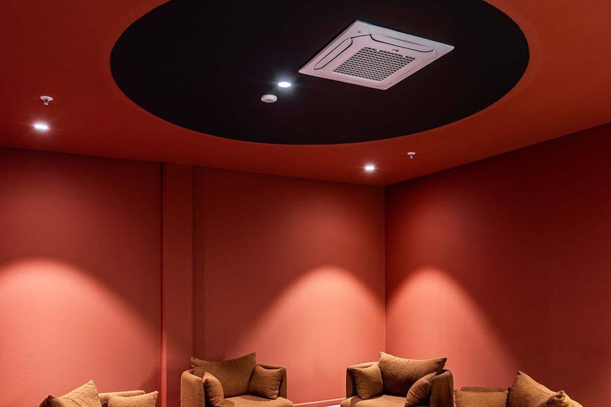A modern, professionally designed lounge area featuring a bold red color scheme, recessed ceiling air conditioning, and integrated fire safety systems.