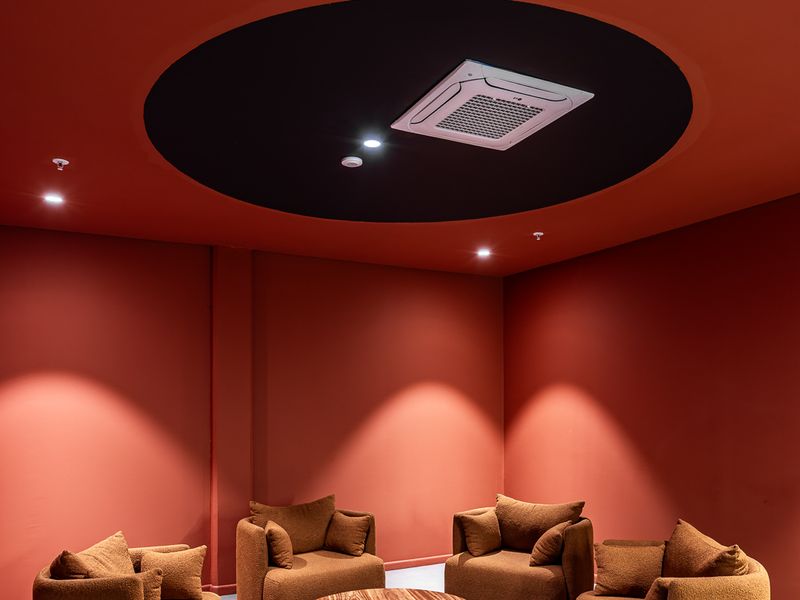 A modern, professionally designed lounge area featuring a bold red color scheme, recessed ceiling air conditioning, and integrated fire safety systems.