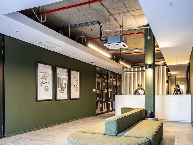 Modern industrial-style reception area featuring an exposed concrete ceiling with red fire piping, sleek tiled flooring, and a professional reception desk.