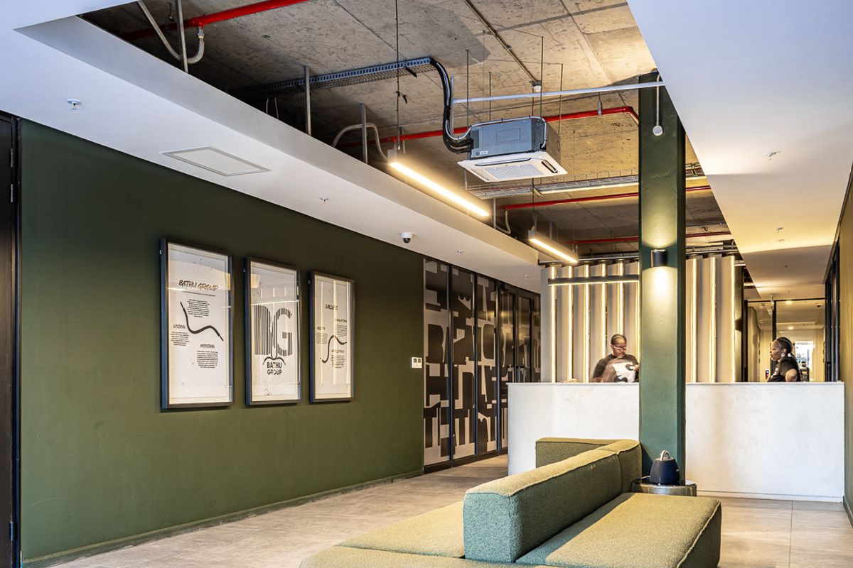 Modern industrial-style reception area featuring an exposed concrete ceiling with red fire piping, sleek tiled flooring, and a professional reception desk.