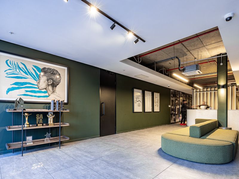 Modern industrial-style office reception area featuring exposed concrete ceilings, track lighting, tiled floors, and a sleek reception desk.