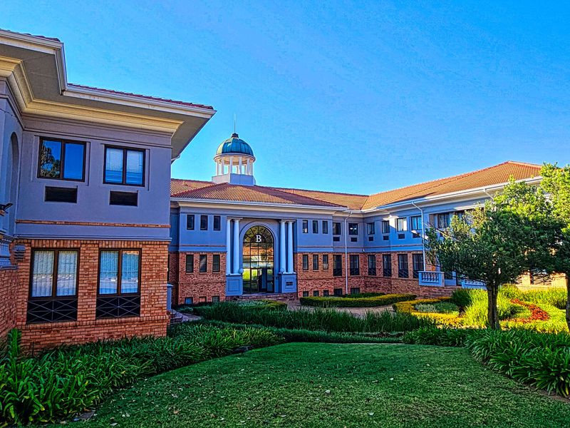 A well-maintained office building exterior featuring a brick and plaster facade, a central cupola, and landscaped garden grounds.