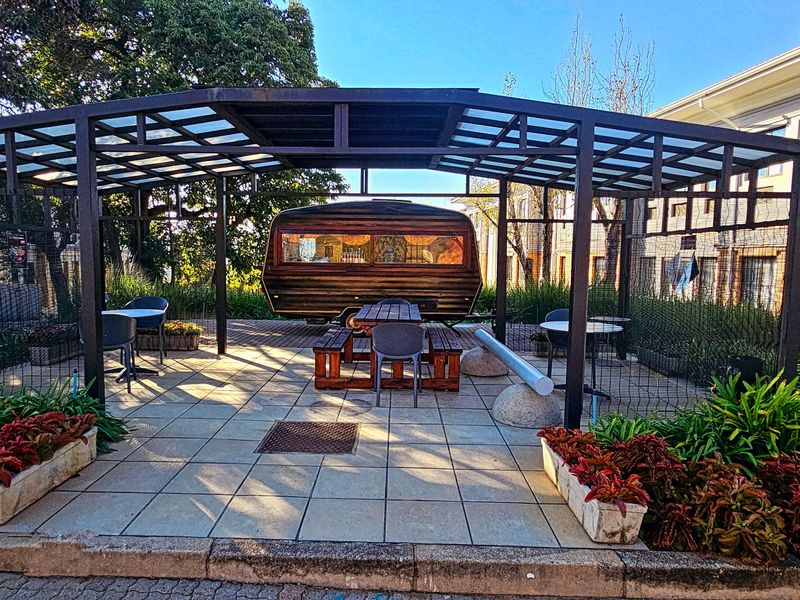 A well-maintained outdoor patio area featuring a modern metal pergola structure, tiled flooring, and integrated garden planters, providing a pleasant communal space.