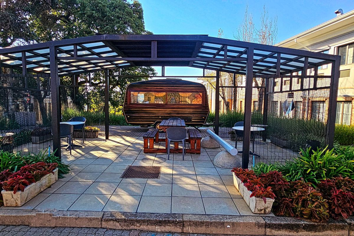 A well-maintained outdoor patio area featuring a modern metal pergola structure, tiled flooring, and integrated garden planters, providing a pleasant communal space.
