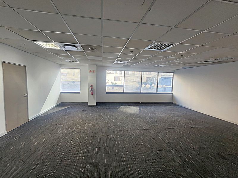 A spacious, empty office suite featuring a suspended ceiling, recessed lighting, large windows for natural light, and durable carpet tile flooring.