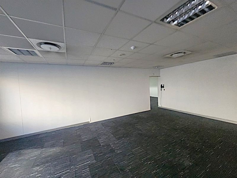 An empty office space featuring a suspended ceiling with recessed lighting, air conditioning vents, and dark carpet tiles.