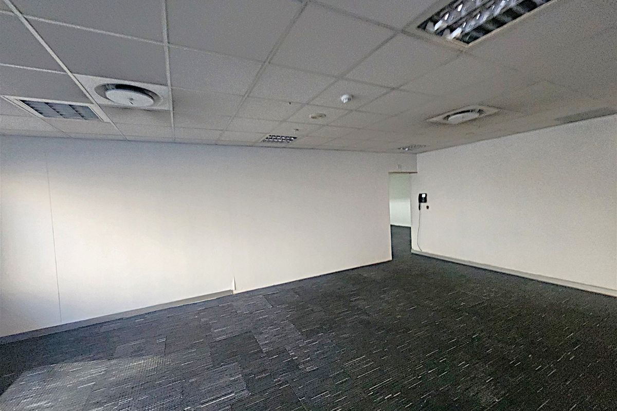 An empty office space featuring a suspended ceiling with recessed lighting, air conditioning vents, and dark carpet tiles.