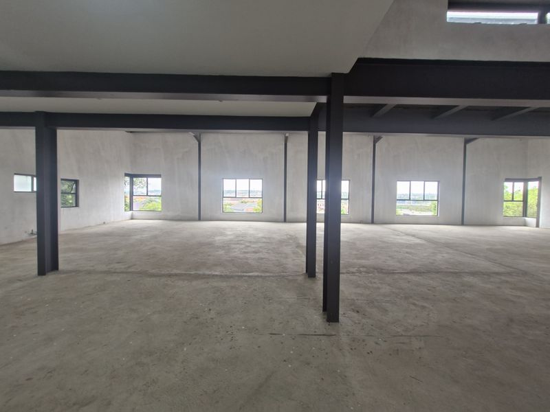 Spacious open-plan office area in shell condition featuring exposed steel structural beams, concrete flooring, and large windows with natural light.