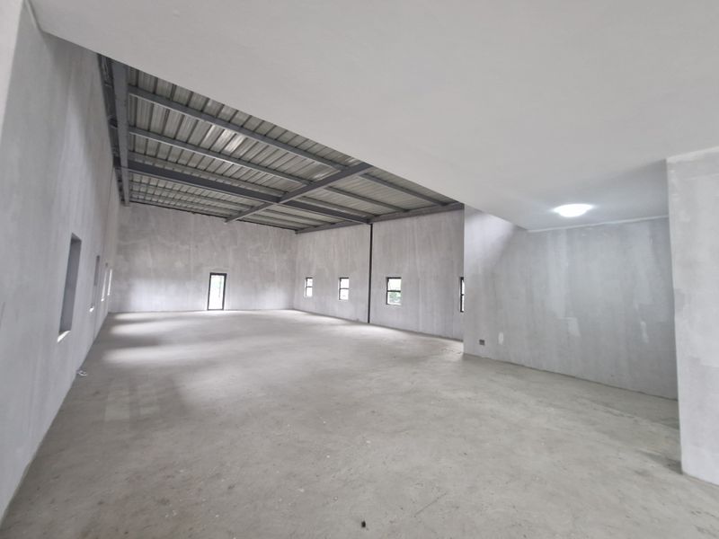 A spacious, open-plan office area featuring exposed steel roof trusses, concrete flooring, and unfinished plastered walls, offering a blank canvas for custom fit-outs.