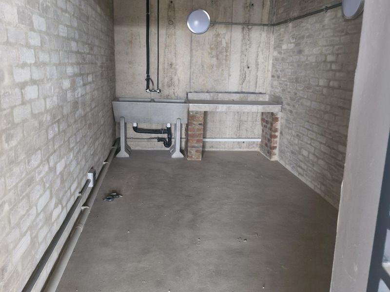 A functional utility space featuring exposed brick and concrete finishes, equipped with a concrete sink and exposed plumbing infrastructure.