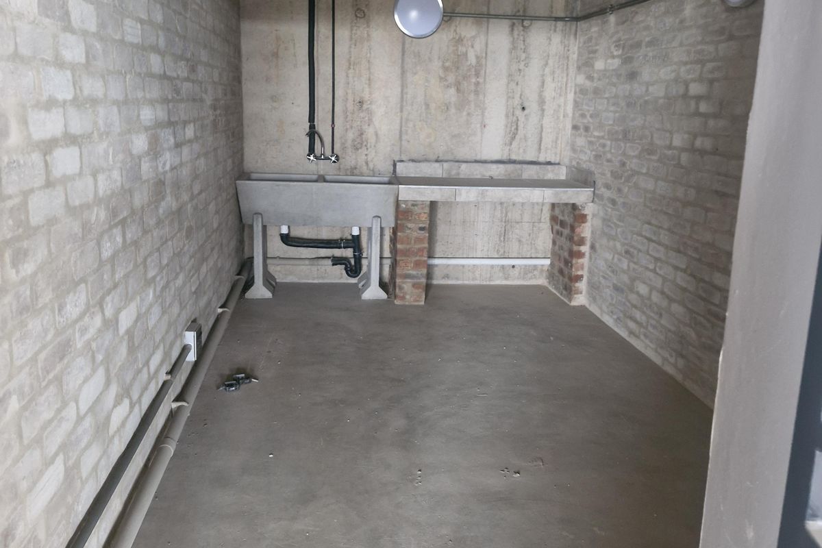 A functional utility space featuring exposed brick and concrete finishes, equipped with a concrete sink and exposed plumbing infrastructure.